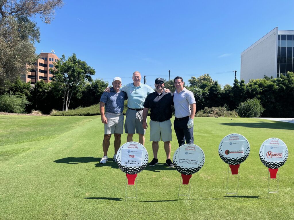 Participants at the Boys & Girls Club of Long Beach "Fore The Kids" golf tournament posing with sponsor signs on the course.