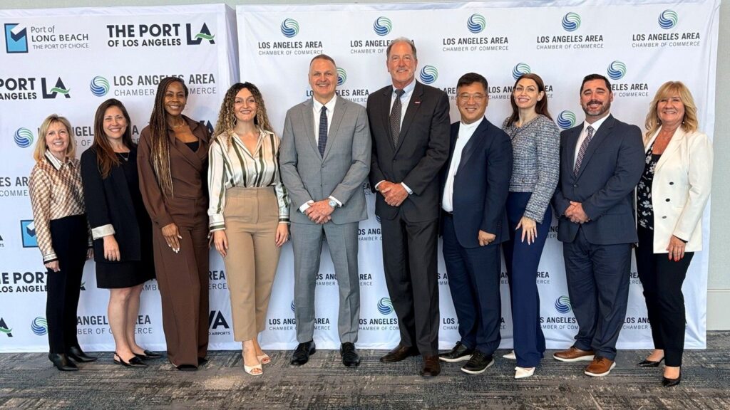 A professional group of ten individuals stands in a row, smiling for a group portrait at an event. They are positioned in front of a white step-and-repeat backdrop featuring repeating logos for "The Port of Los Angeles," "Port of Long Beach," and the "Los Angeles Area Chamber of Commerce."